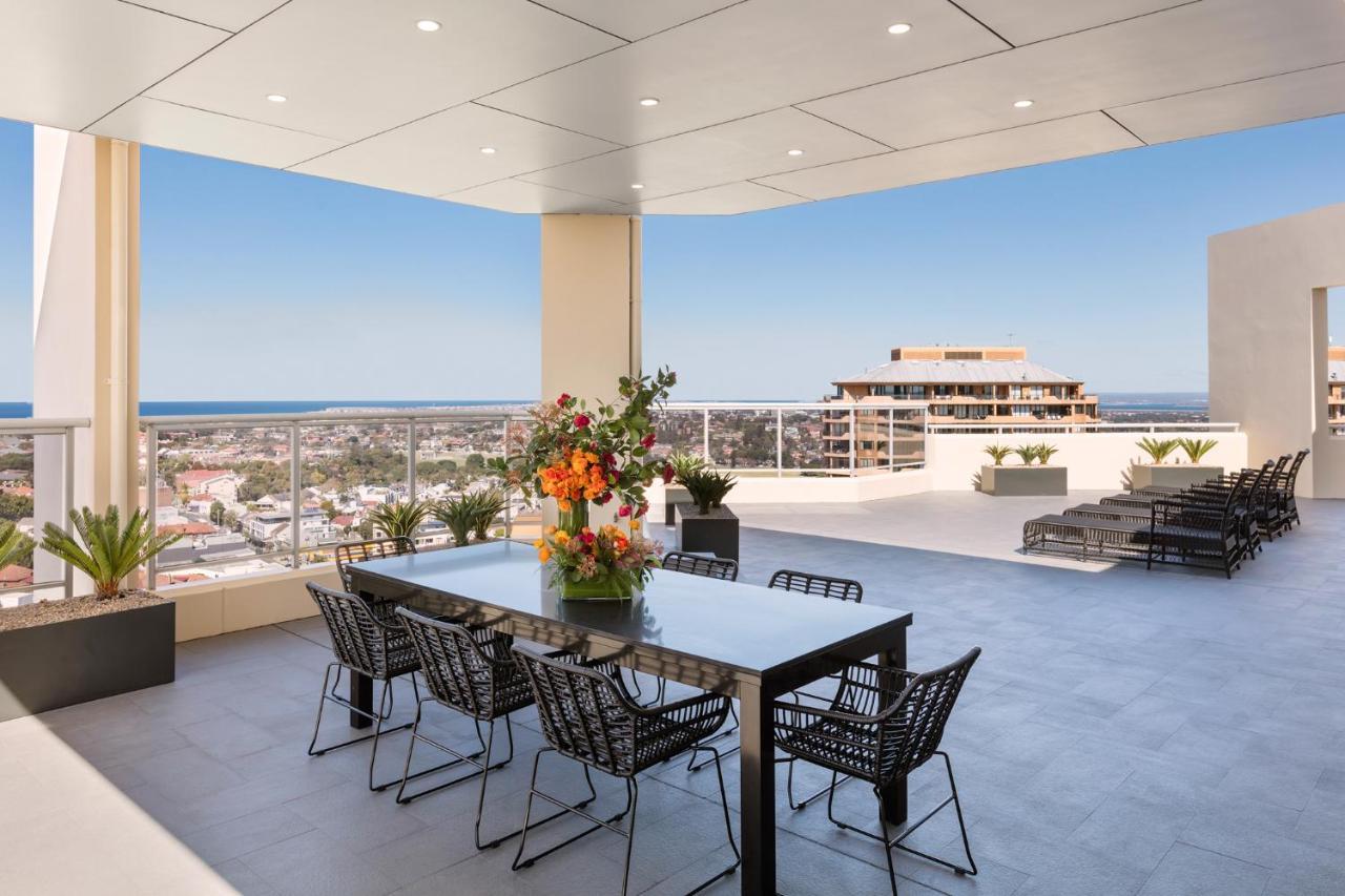 เมอริตัน สวีท บอนดี จังค์ชั่น Hotel ซิดนีย์ ภายนอก รูปภาพ The photo shows a stylish outdoor terrace or balcony area, featuring a long dining table surrounded by several black wire chairs. The table has a centerpiece of vibrant flowers. The space is well-lit, with a clear view of the horizon in the backgroun
