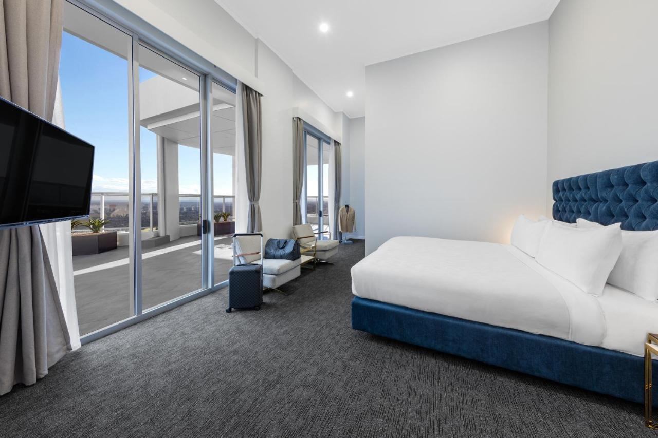 เมอริตัน สวีท บอนดี จังค์ชั่น Hotel ซิดนีย์ ภายนอก รูปภาพ The photo shows a modern and spacious hotel room. It features a large bed with a blue headboard, a flat-screen TV mounted on the wall, and a cozy seating area with a chair and small table. The room has large windows that offer natural light and a vie