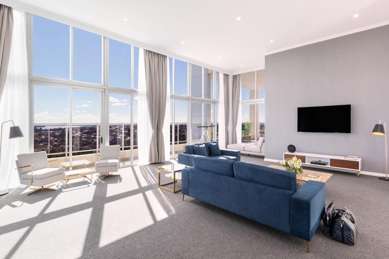 เมอริตัน สวีท บอนดี จังค์ชั่น Hotel ซิดนีย์ ภายนอก รูปภาพ The photo shows a bright and modern living room with large floor-to-ceiling windows that provide a view of the outdoors. The space features a blue sofa in the center, complemented by light-colored armchairs nearby. There are light curtains hanging by