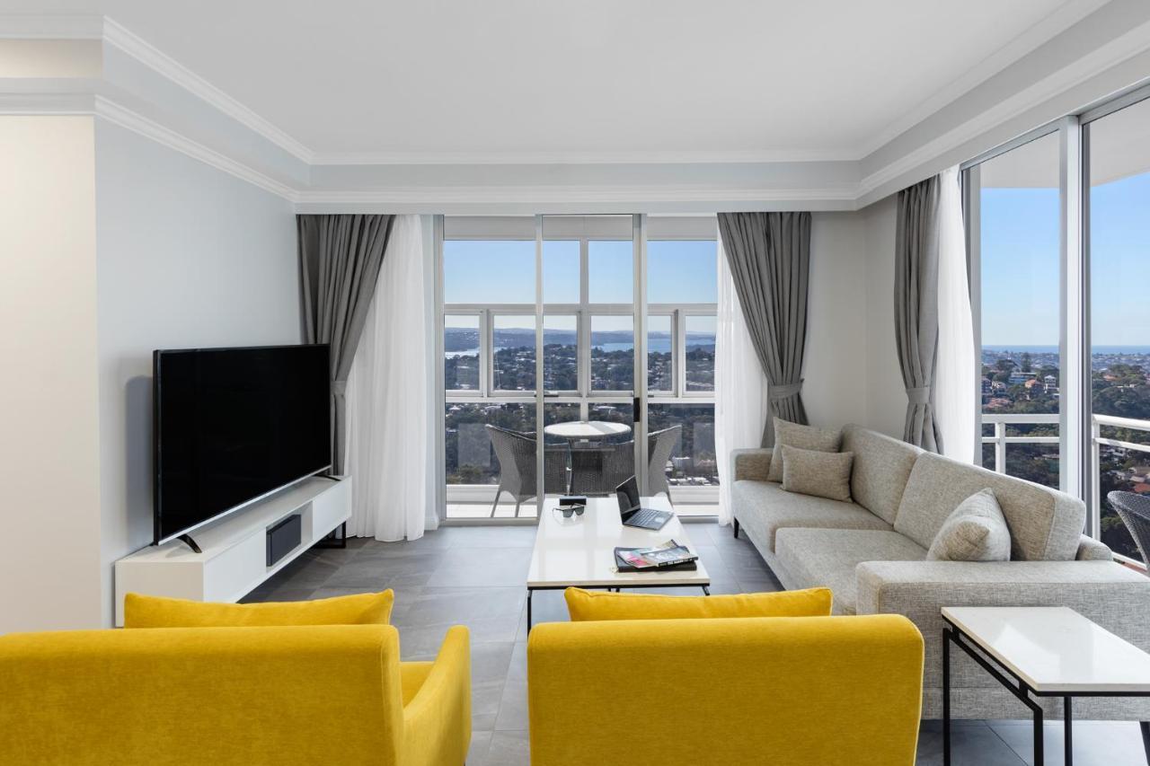 เมอริตัน สวีท บอนดี จังค์ชั่น Hotel ซิดนีย์ ภายนอก รูปภาพ The photo depicts a modern living room space with large windows that offer a view of the outside. The decor is minimalist and stylish, featuring a light color palette. 

In the center, there are two bright yellow chairs facing each other. A sleek, re