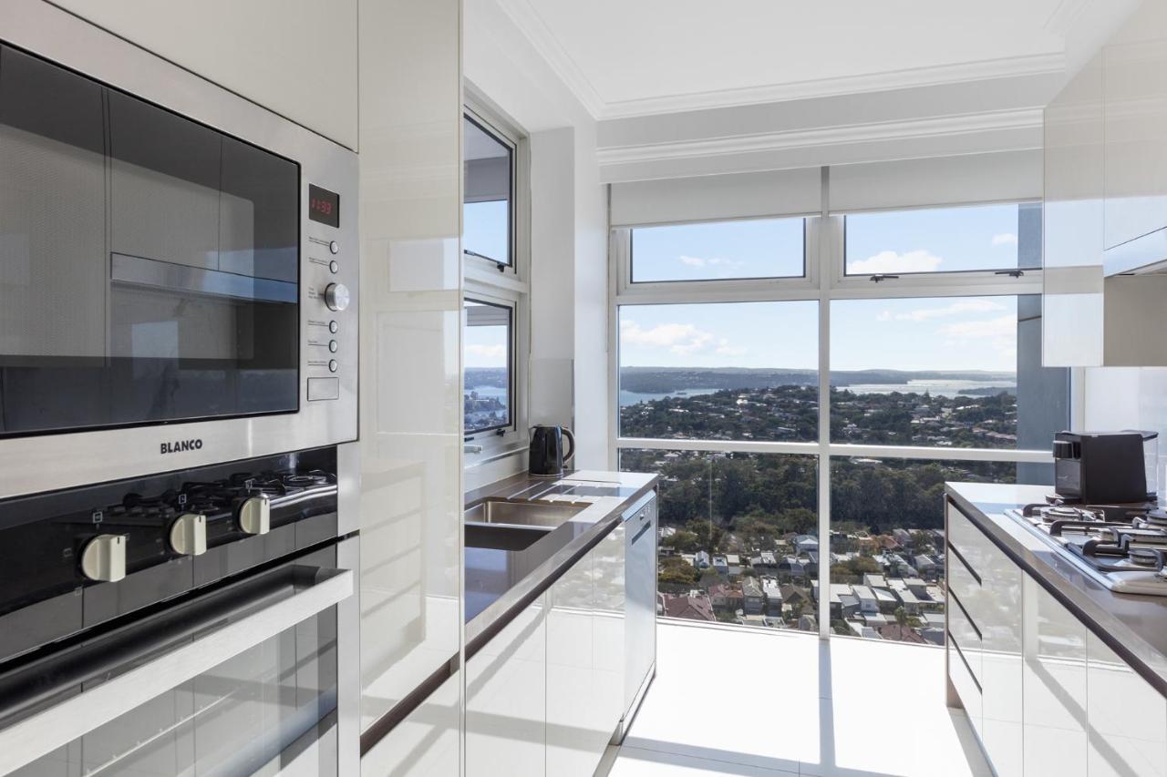 เมอริตัน สวีท บอนดี จังค์ชั่น Hotel ซิดนีย์ ภายนอก รูปภาพ The photo shows a modern kitchen with sleek, shiny white cabinets and a large window that offers a panoramic view of the outside landscape. The kitchen features built-in appliances, including an oven and a stove, with a stylish countertop. The spacio