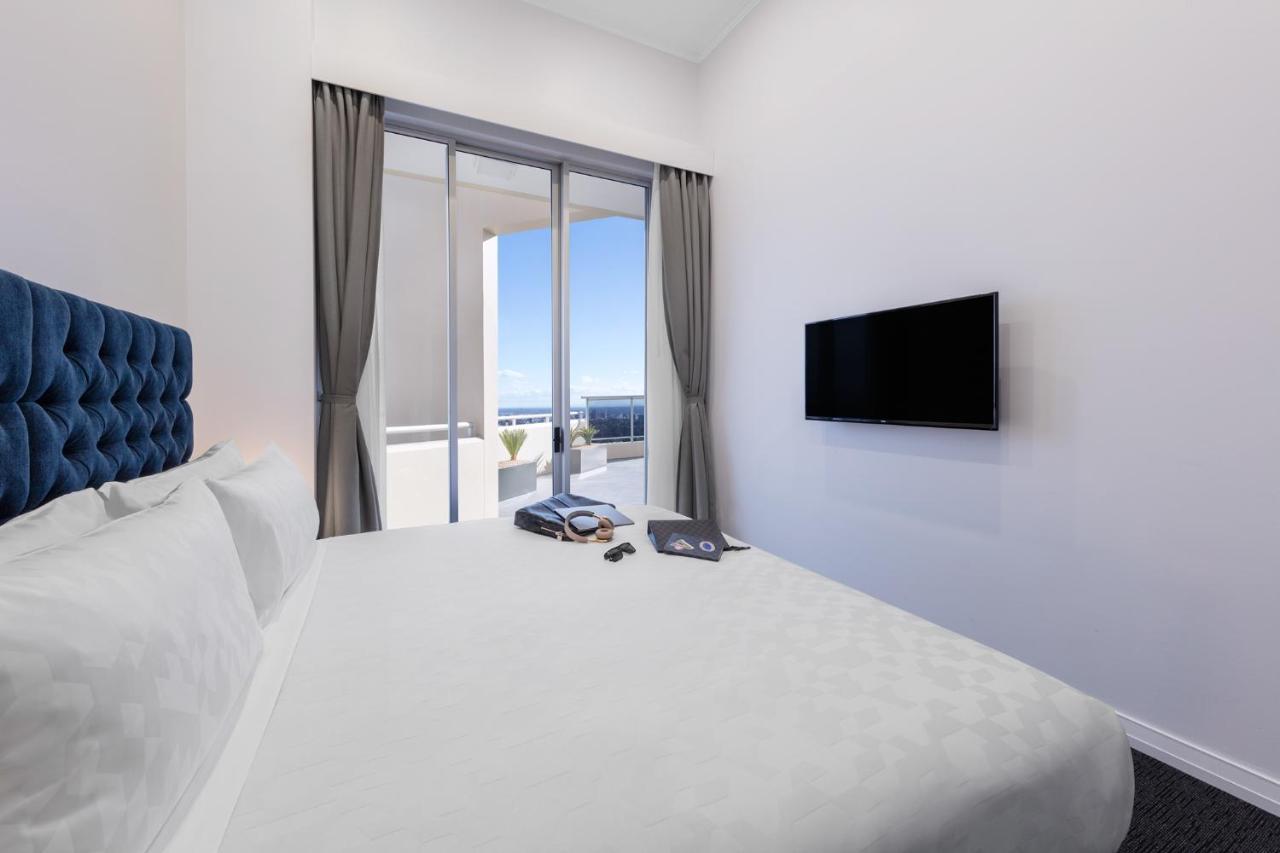 เมอริตัน สวีท บอนดี จังค์ชั่น Hotel ซิดนีย์ ภายนอก รูปภาพ The photo shows a modern hotel room with a large, comfortable bed featuring a blue tufted headboard. There are light-colored walls, and the room is decorated simply. A flat-screen TV is mounted on the wall opposite the bed. The room has large glass d