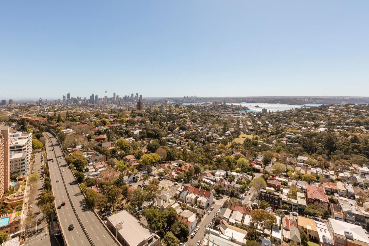 เมอริตัน สวีท บอนดี จังค์ชั่น Hotel ซิดนีย์ ภายนอก รูปภาพ The photo captures a panoramic view of a vibrant urban landscape. In the foreground, there are residential areas with various houses and greenery, showcasing a suburban environment. In the background, the skyline of a city can be seen, featuring tall