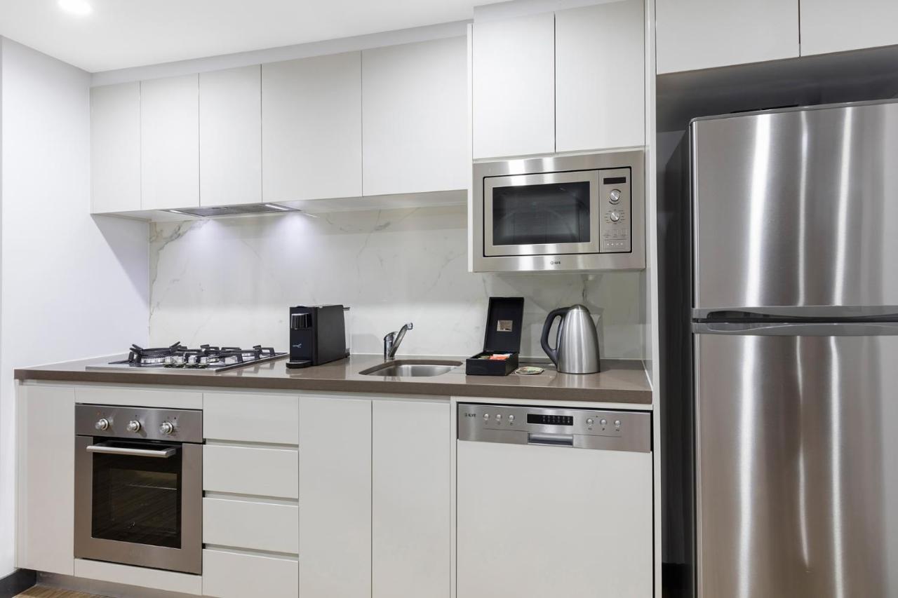 เมอริตัน สวีท บอนดี จังค์ชั่น Hotel ซิดนีย์ ภายนอก รูปภาพ The photo shows a modern kitchen with a sleek, minimalist design. It features white cabinetry and a countertop that blends with the overall aesthetic. 

Key elements include:

- A stainless steel refrigerator on the right.
- An oven with a gas cookto