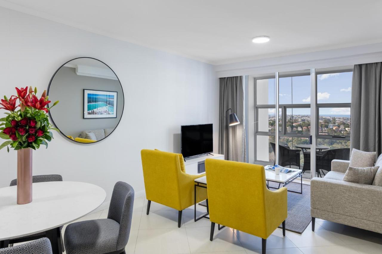 เมอริตัน สวีท บอนดี จังค์ชั่น Hotel ซิดนีย์ ภายนอก รูปภาพ The photo shows a modern living space with a stylish design. There are two bright yellow chairs facing a small glass table, and a comfortable beige sofa to the right. A TV is positioned on the wall in front of the chairs. To the left, there's a dinin