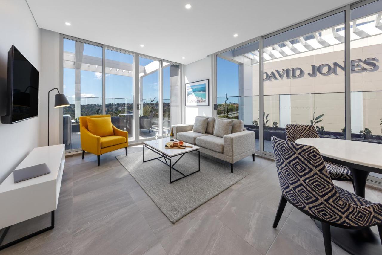 เมอริตัน สวีท บอนดี จังค์ชั่น Hotel ซิดนีย์ ภายนอก รูปภาพ The photo shows a modern living space that features large windows allowing ample natural light. The room is furnished with a gray sofa and a bright yellow armchair, along with a coffee table in between. There’s a decorative bowl with fruits on the ta