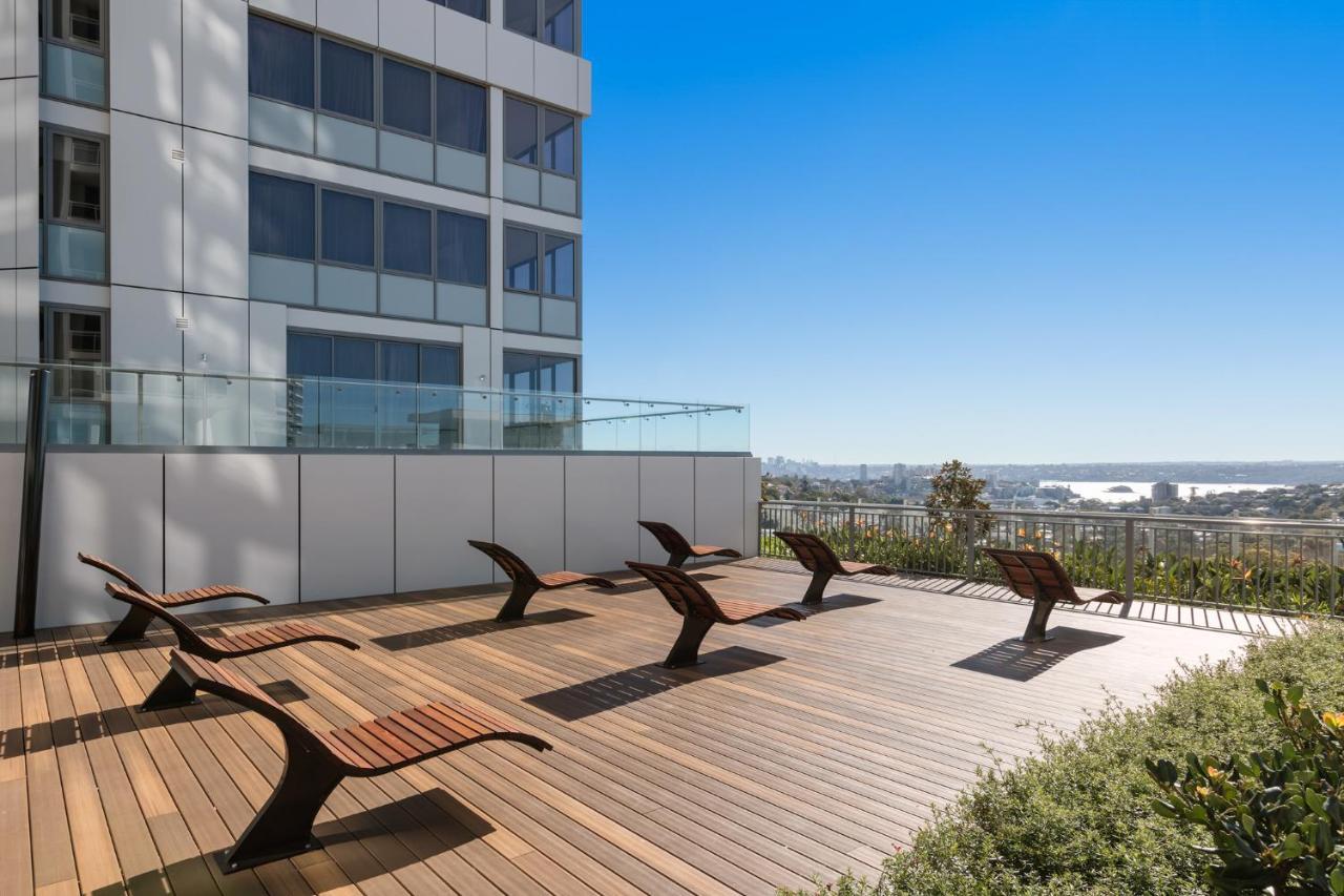 เมอริตัน สวีท บอนดี จังค์ชั่น Hotel ซิดนีย์ ภายนอก รูปภาพ The photo shows a rooftop or outdoor area with a wooden deck. There are several modern lounge chairs arranged neatly, facing a clear sky and a panoramic view of the surrounding landscape. In the background, there is a tall building with large windows