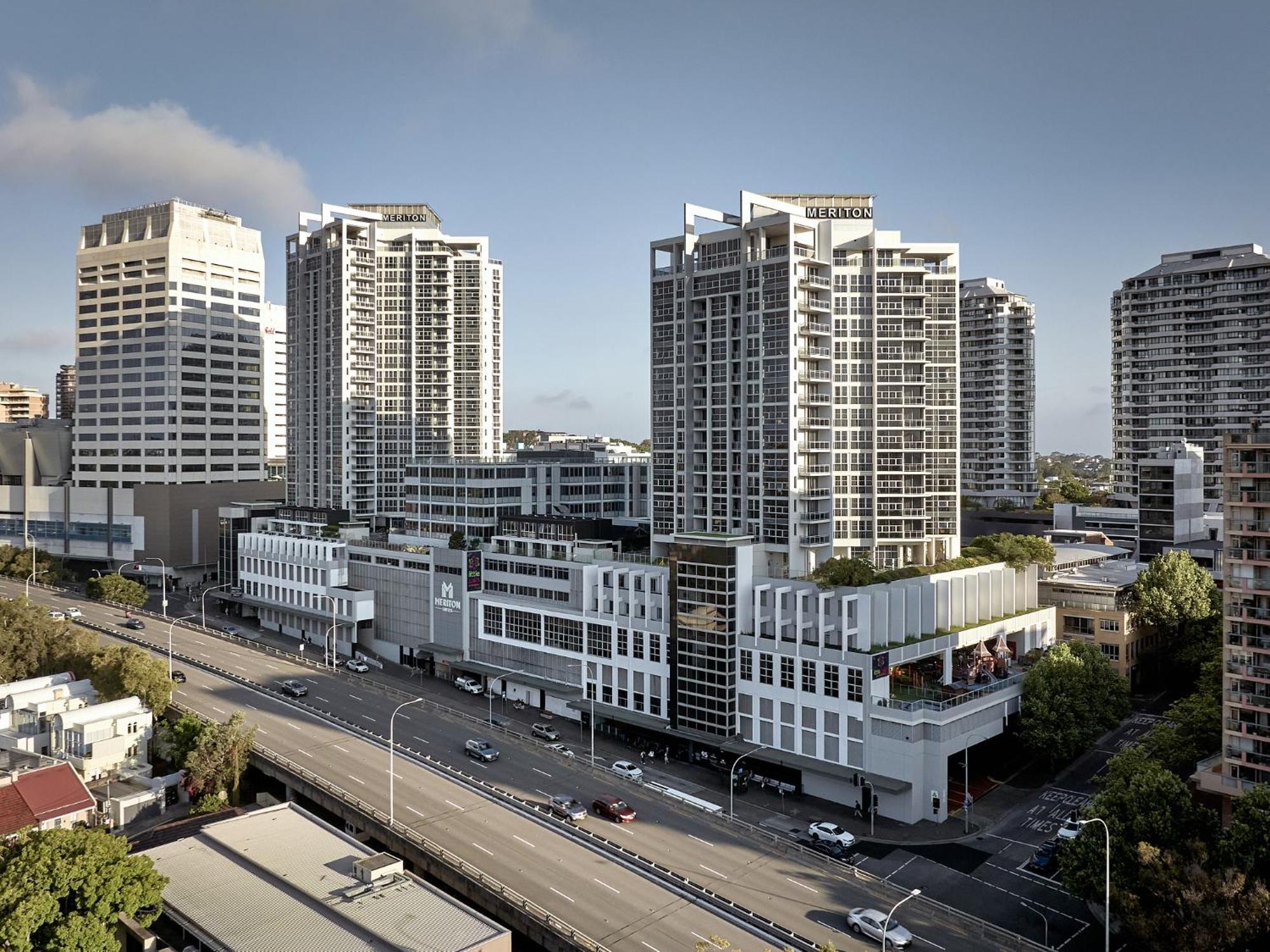เมอริตัน สวีท บอนดี จังค์ชั่น Hotel ซิดนีย์ ภายนอก รูปภาพ The photo shows a cityscape featuring several tall modern buildings, likely apartments or office complexes. In the foreground, there is a road lined with cars, and the architecture of the buildings varies, with some having sleek glass facades and oth