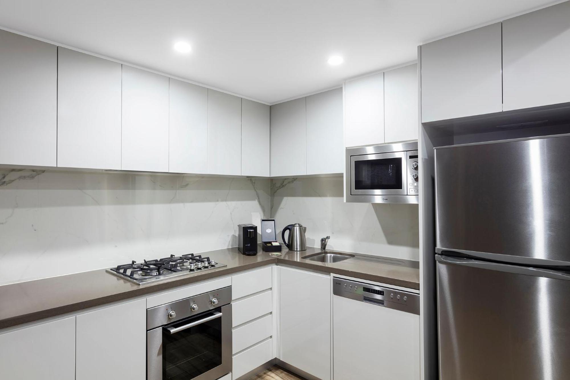 เมอริตัน สวีท บอนดี จังค์ชั่น Hotel ซิดนีย์ ภายนอก รูปภาพ The photo shows a modern kitchen featuring a minimalist design. It has light-colored cabinetry, a countertop, and stainless steel appliances. The appliances include a gas stove with multiple burners, an oven, a microwave, a kettle, and a refrigerator