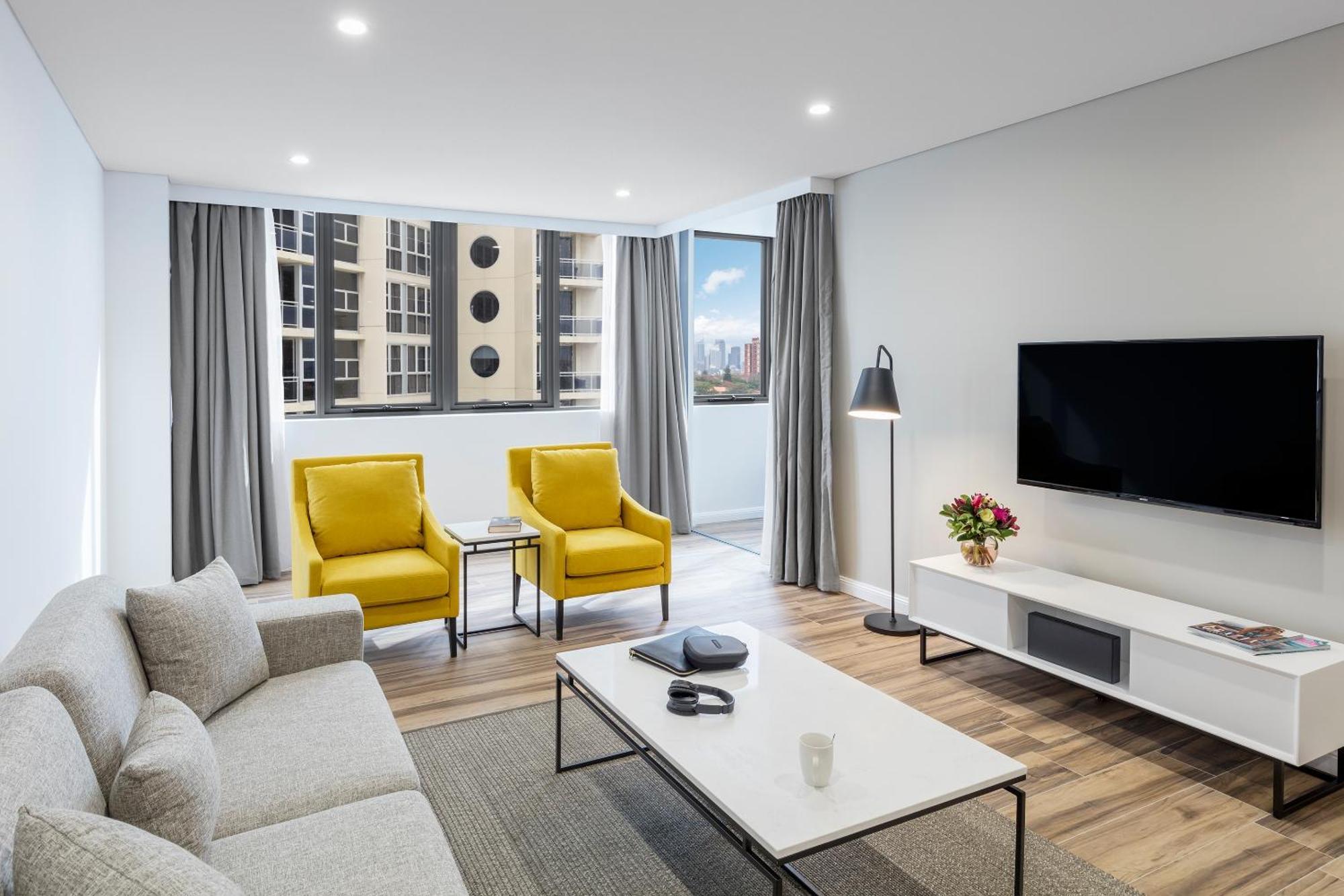 เมอริตัน สวีท บอนดี จังค์ชั่น Hotel ซิดนีย์ ภายนอก รูปภาพ The photo shows a modern, well-lit living room. It features a light gray sofa with a textured fabric. There are two bright yellow armchairs positioned near a window, which allows natural light to enter the space. The room has light gray curtains and 